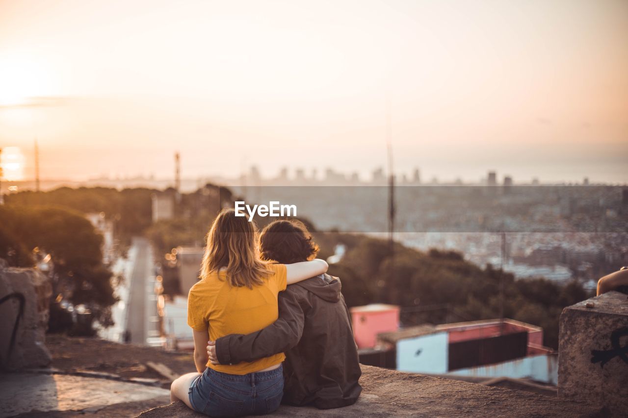 Rear view of couple looking at cityscape against sky during sunset
