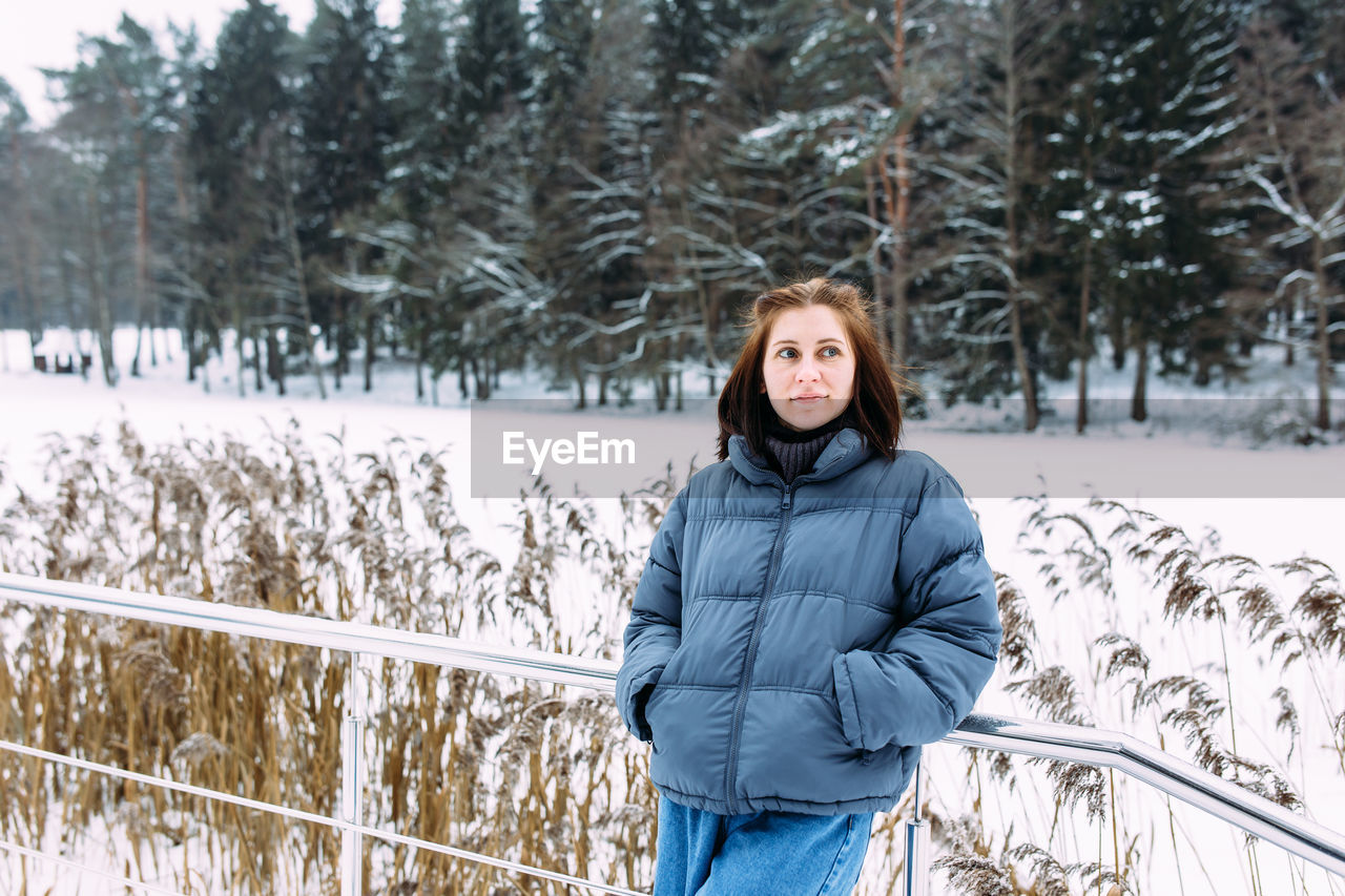 portrait of young woman standing on snow covered field during winter