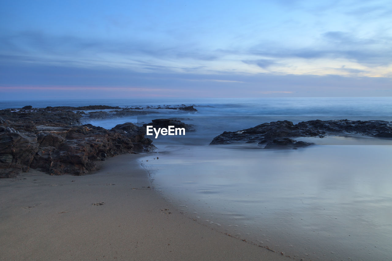 View of calm beach against cloudy sky