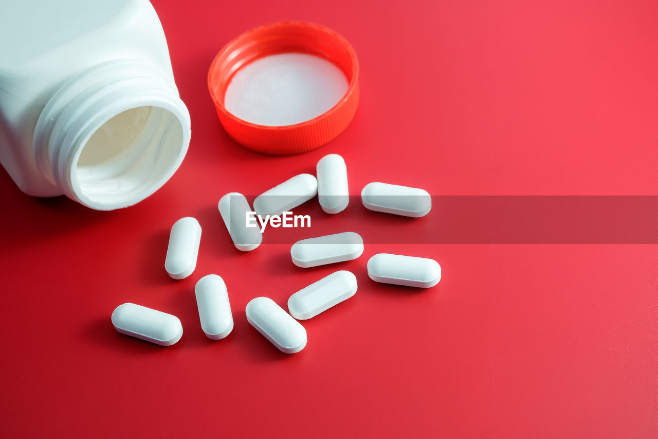 Close-up of pills by bottle against red background