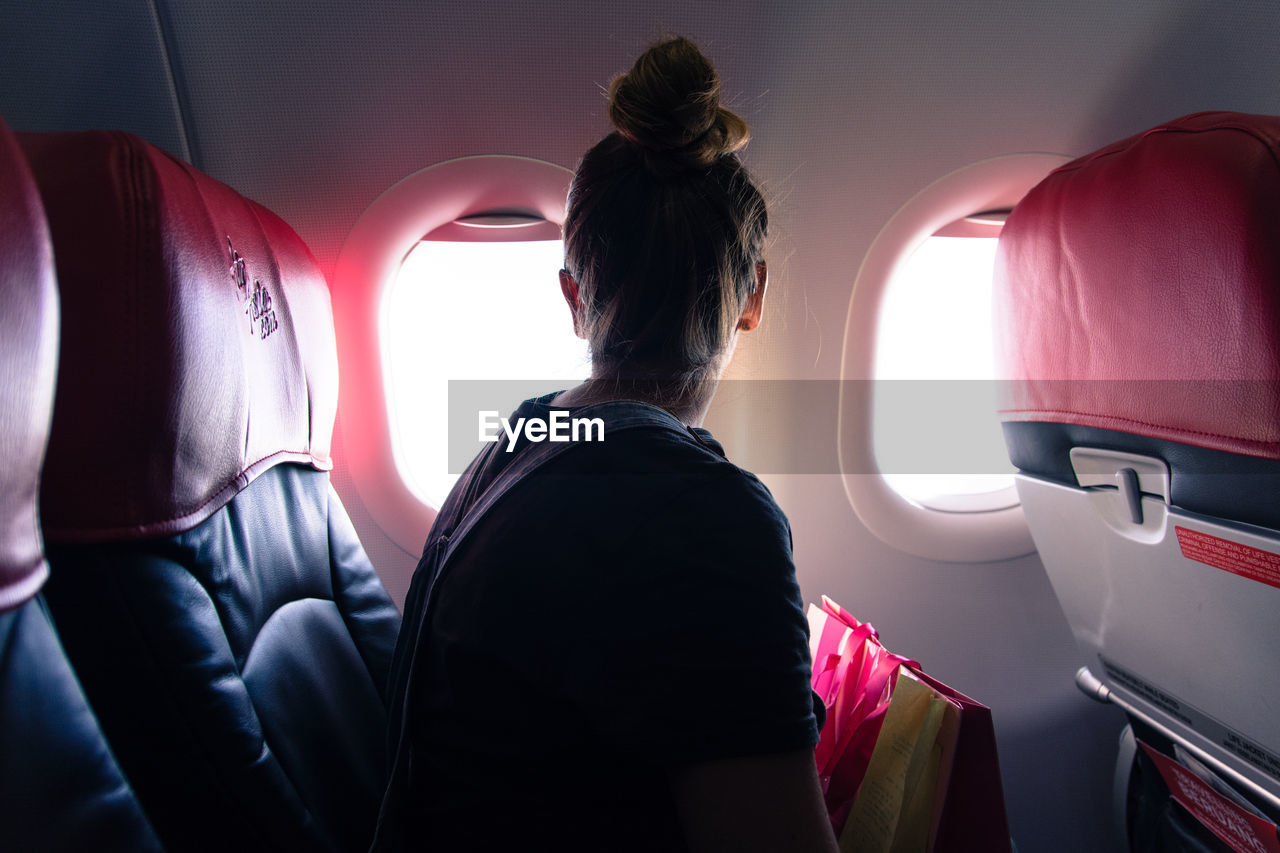 Woman looking through window while traveling in airplane