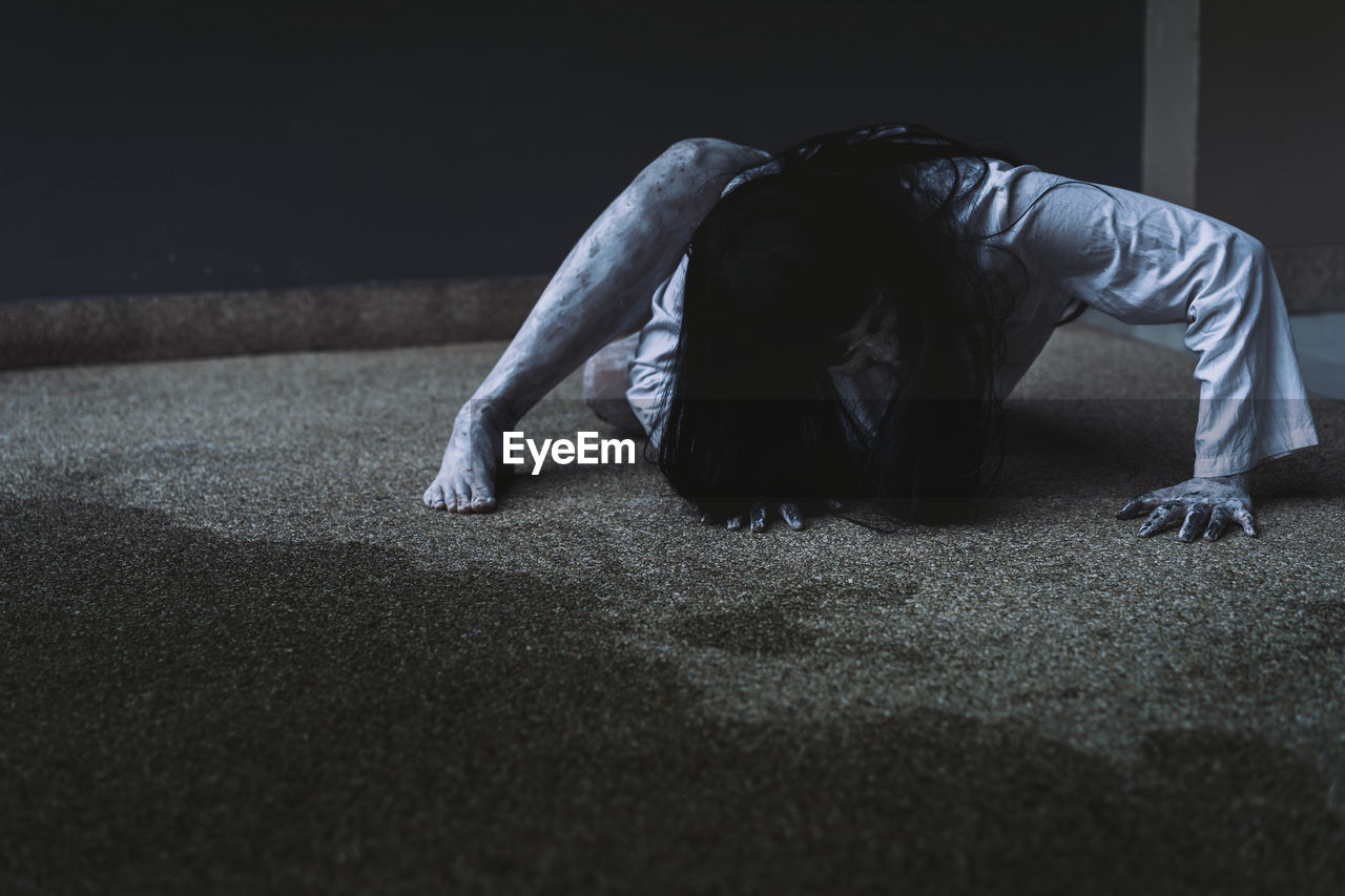 Spooky young woman crouching on floor against wall