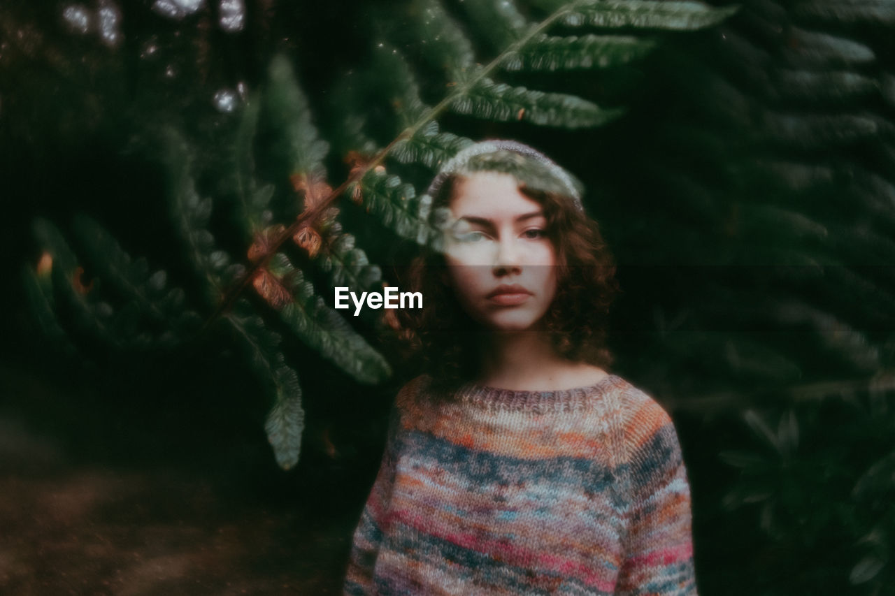 Girl standing behind leaves in sweater and hat