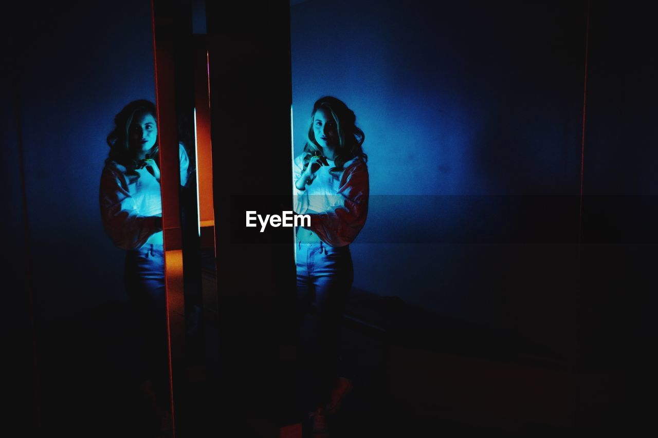 Young woman standing against illuminated light and mirror in darkroom