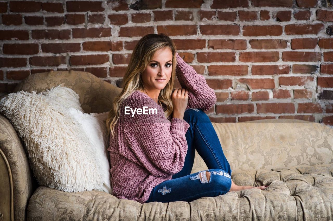 PORTRAIT OF YOUNG WOMAN SITTING ON BRICK WALL