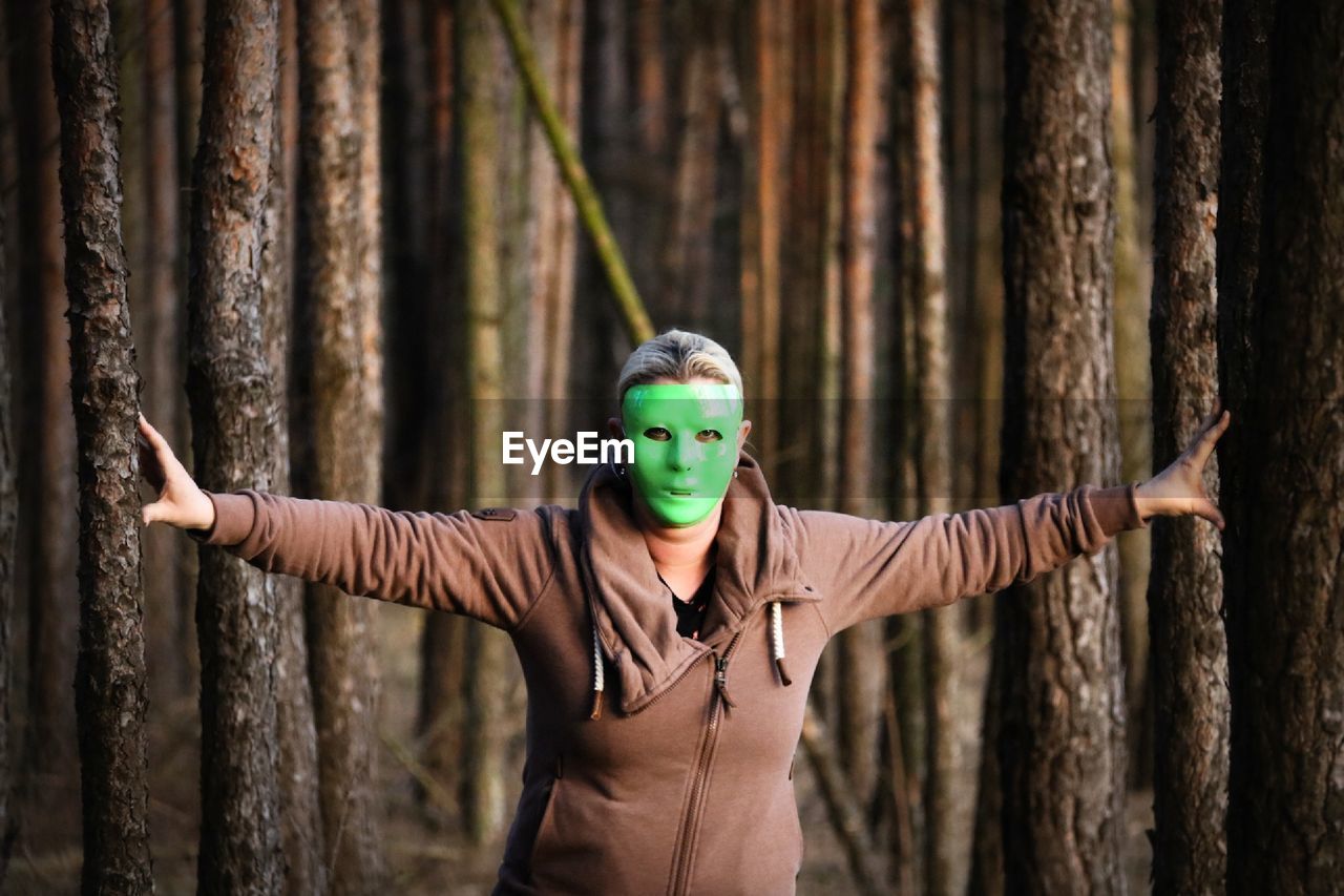 Portrait of woman wearing mask with arms outstretched standing in forest