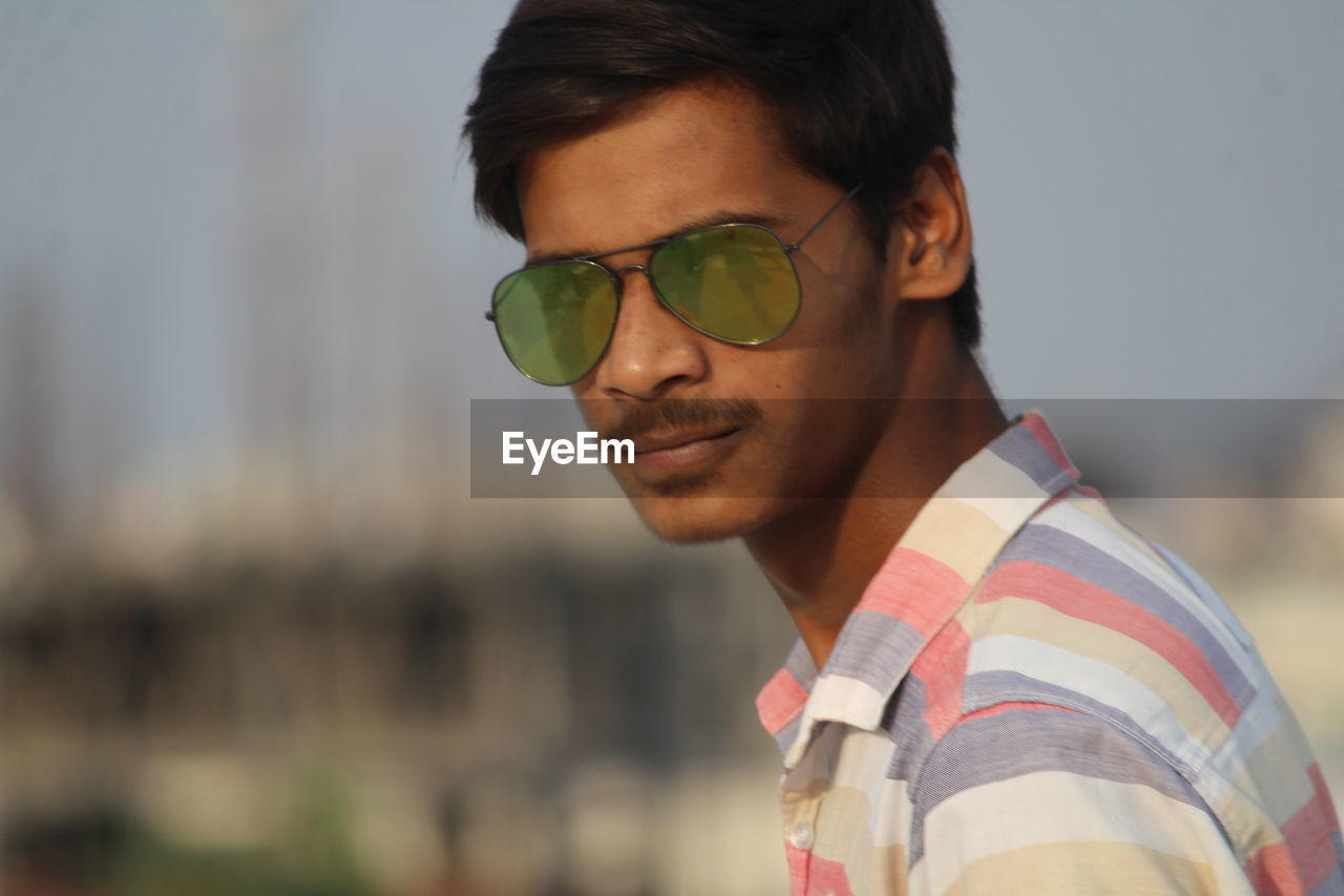 PORTRAIT OF SMILING YOUNG MAN WEARING SUNGLASSES OUTDOORS