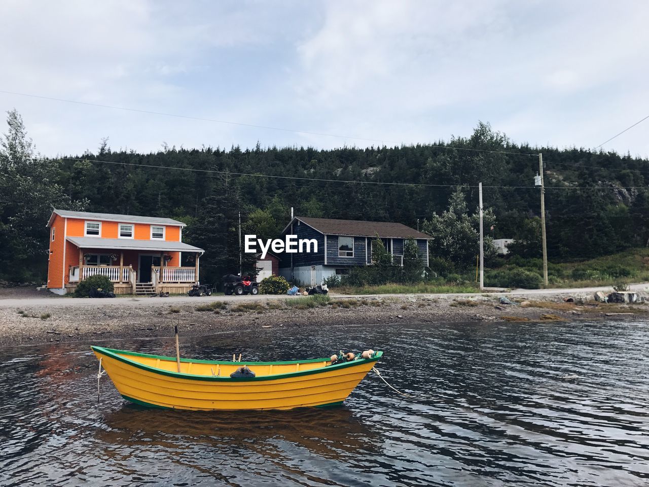 YELLOW BOATS MOORED ON HOUSE BY TREES AGAINST SKY