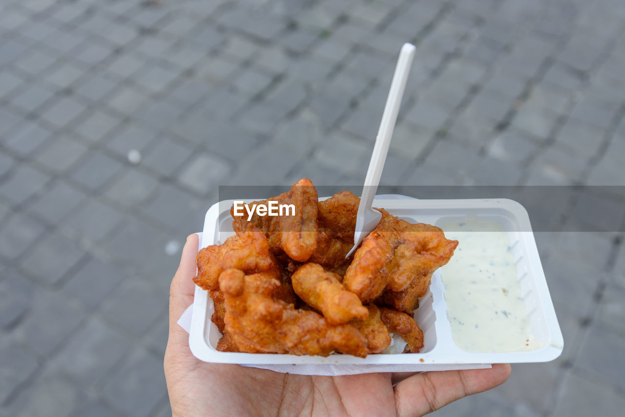 Hand hold kibbeling, deep fried battered fish, and white mayonnaise sauce on side.