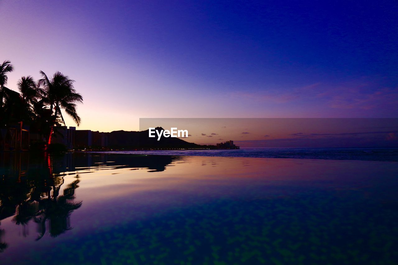 SCENIC VIEW OF SWIMMING POOL BY SEA AGAINST SKY DURING SUNSET