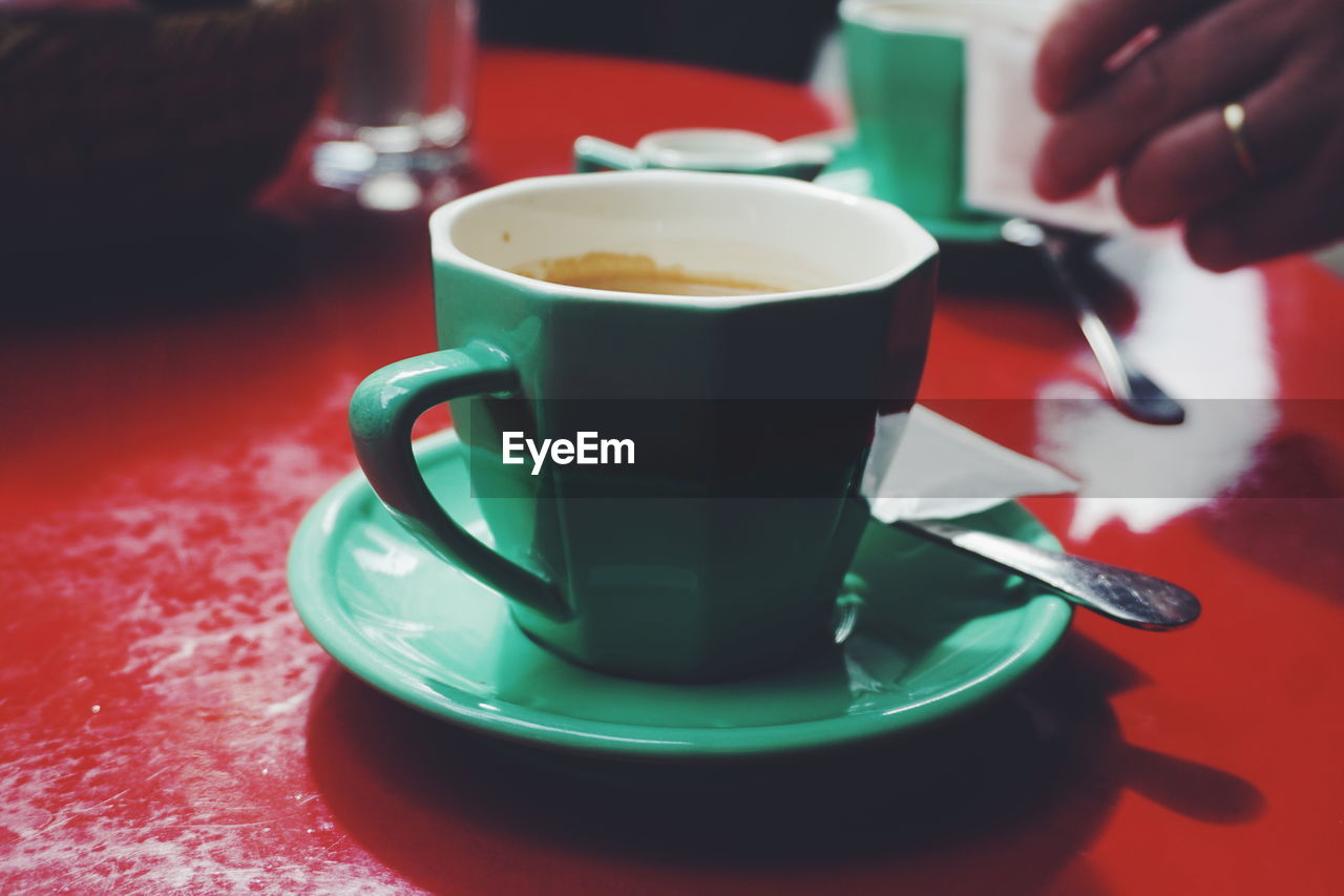 Close-up of coffee cup on table with hand in background