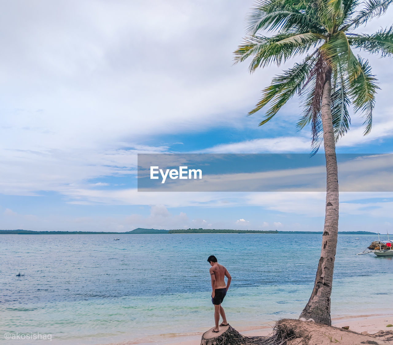 Shirtless man standing on tree at beach against sky