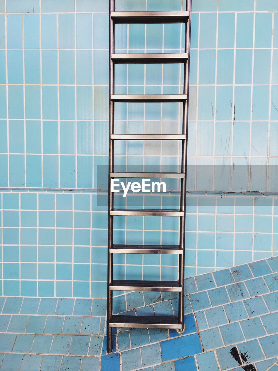 Metallic ladder against blue tile wall in abandoned swimming pool