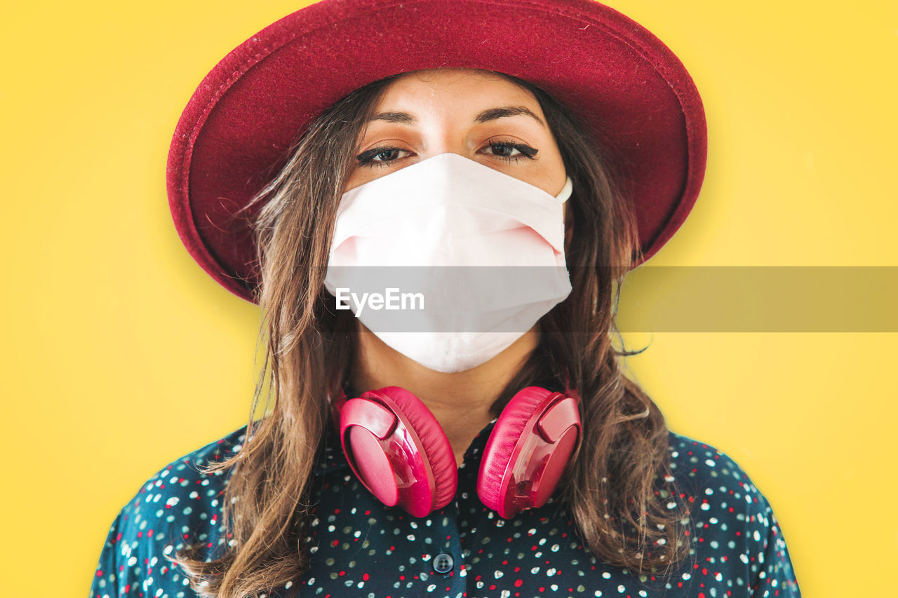 Portrait of woman wearing mask and hat against yellow background