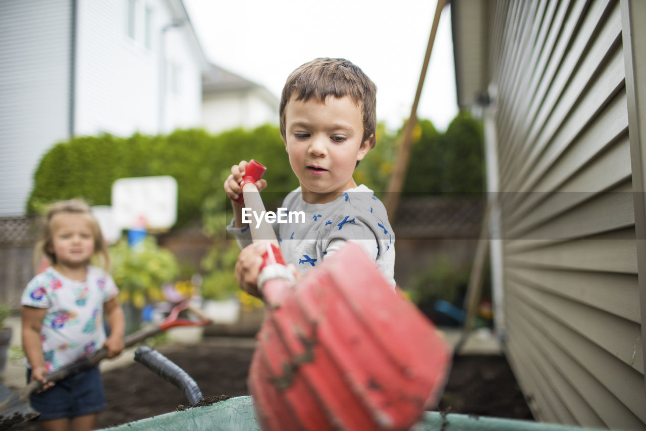 Young boy using red shovel in his backyard.