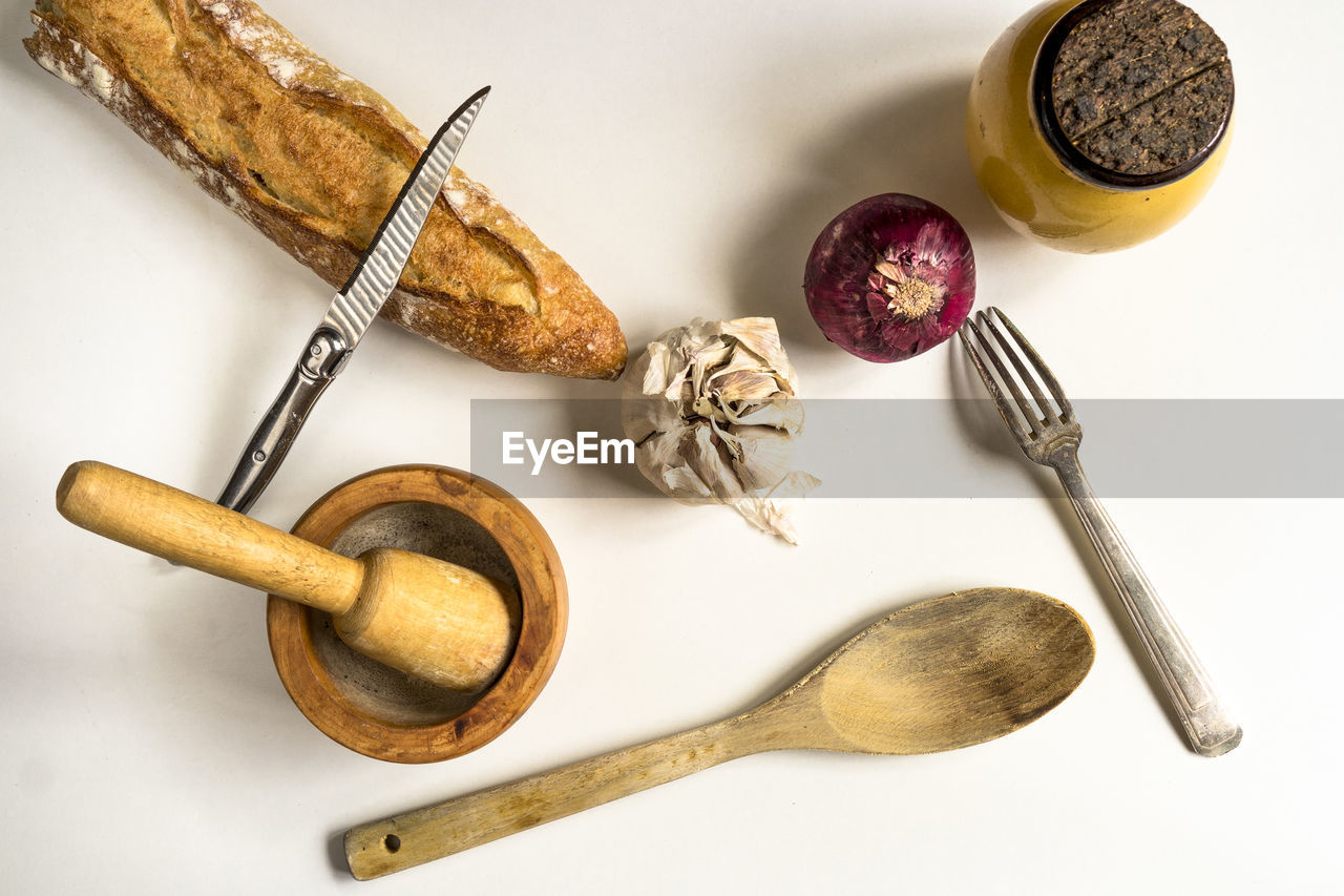 Directly above shot of bread with onion and garlic by kitchen utensils against white background