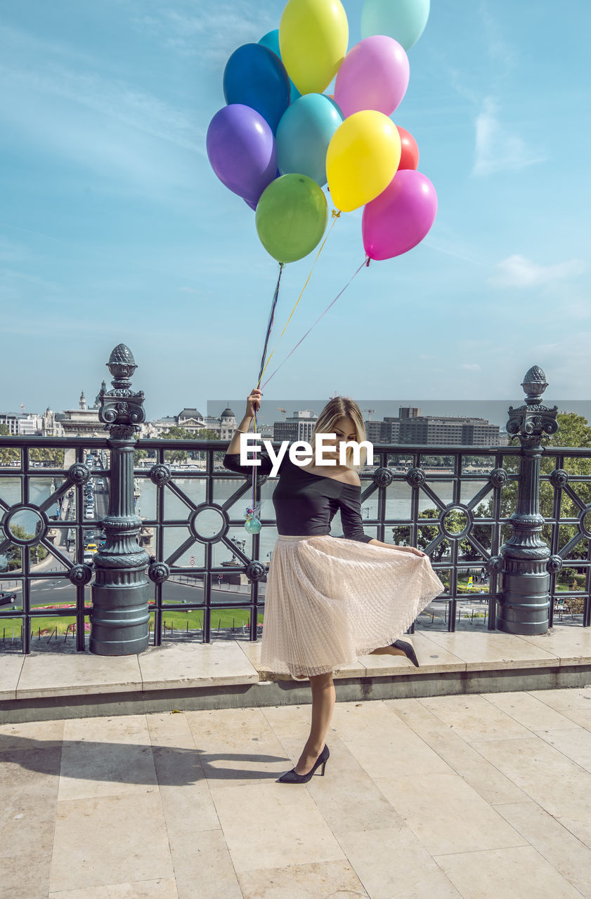 Woman with colorful balloons on walkway against sky in city