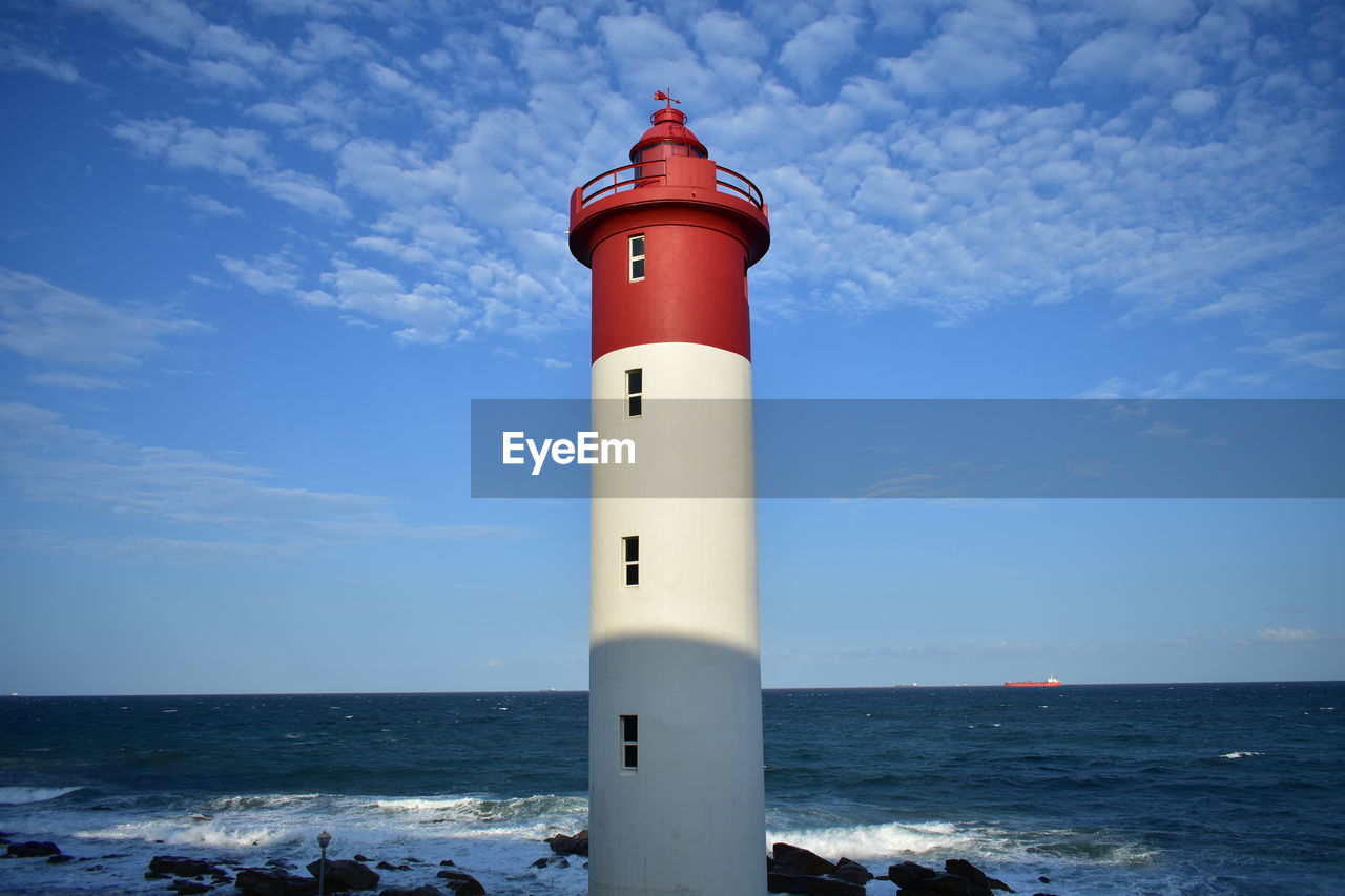 Lighthouse by sea against blue sky