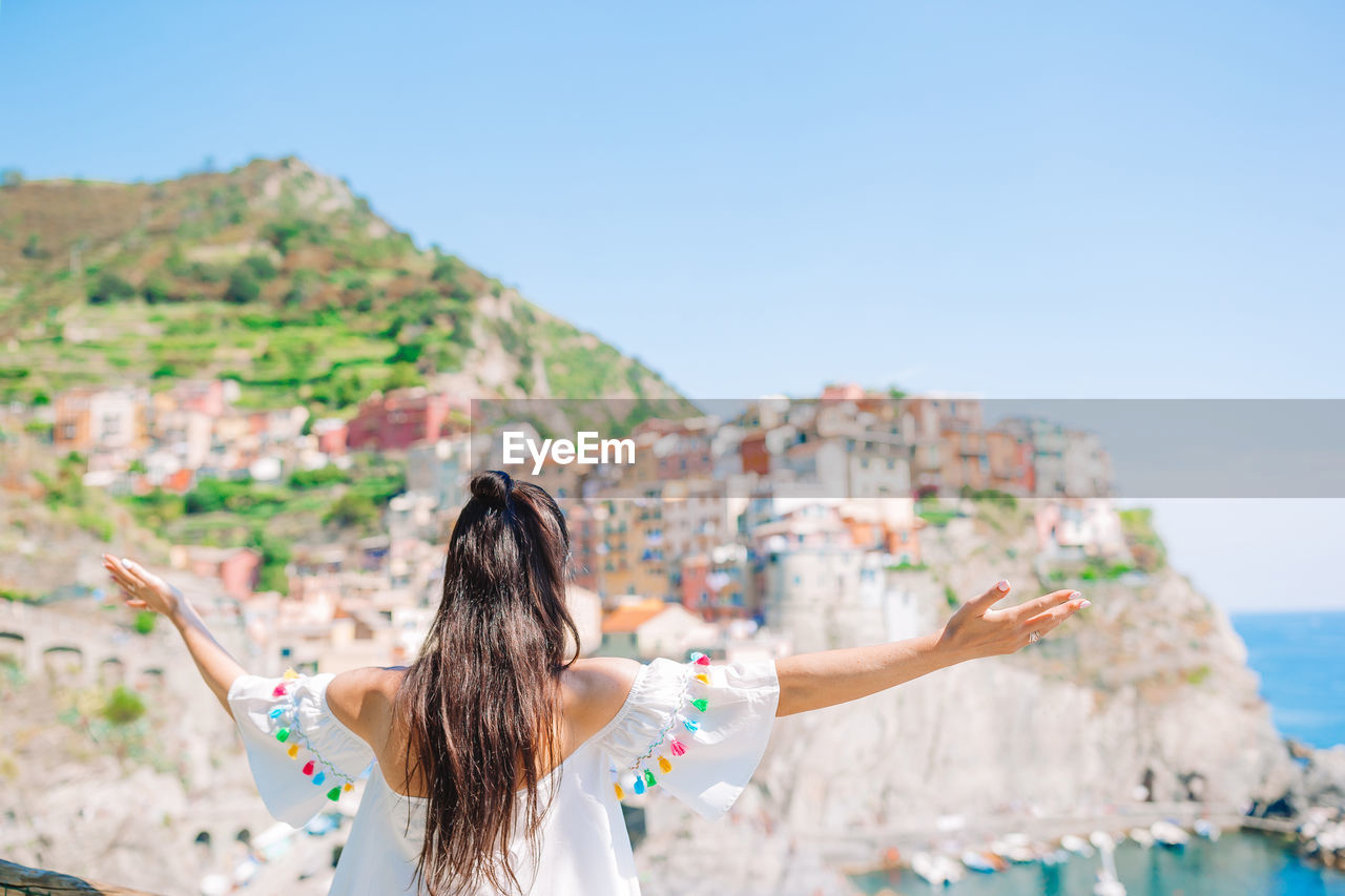 REAR VIEW OF WOMAN WITH ARMS OUTSTRETCHED AGAINST SKY