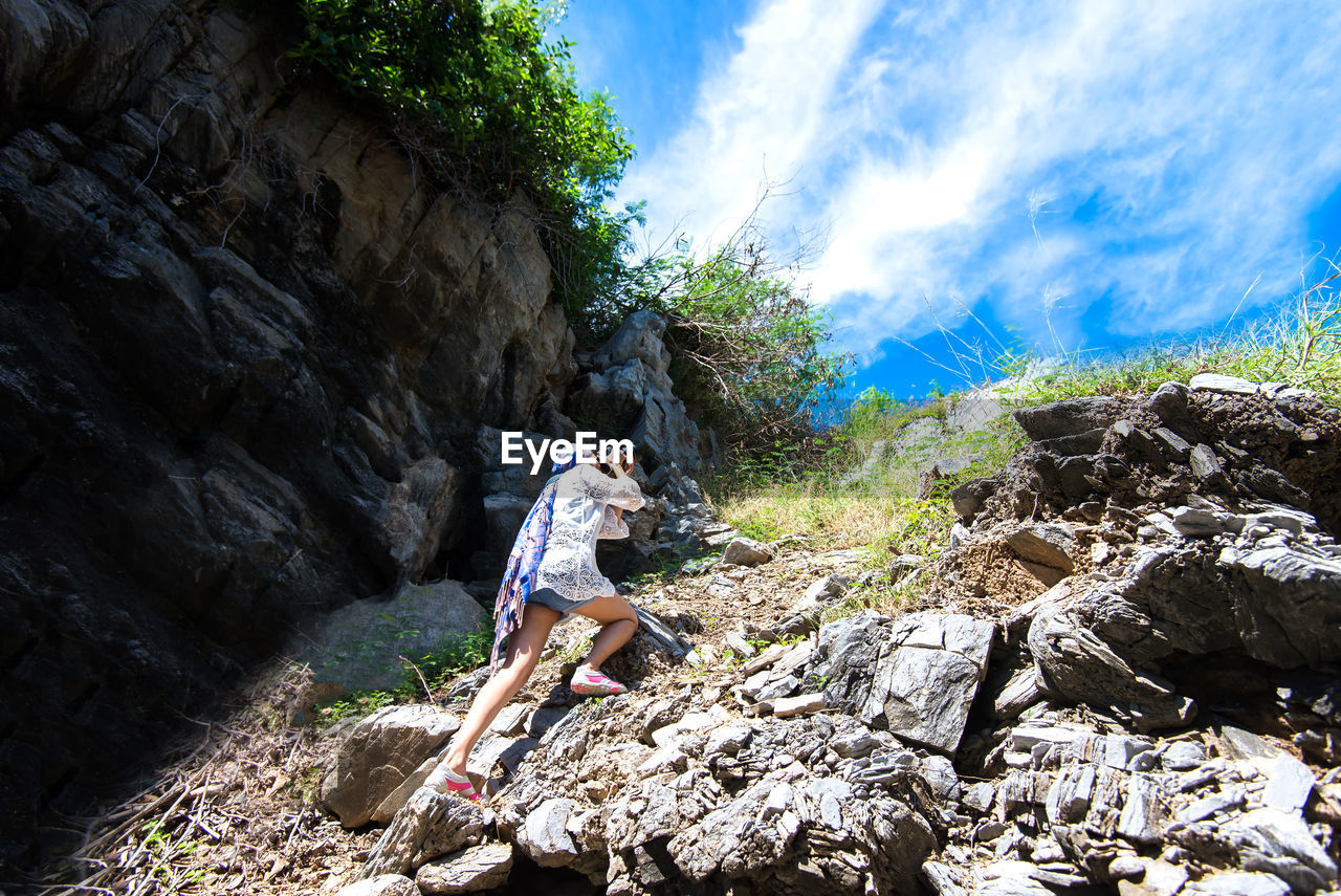 Low angle view of woman photographing while standing on mountain against sky