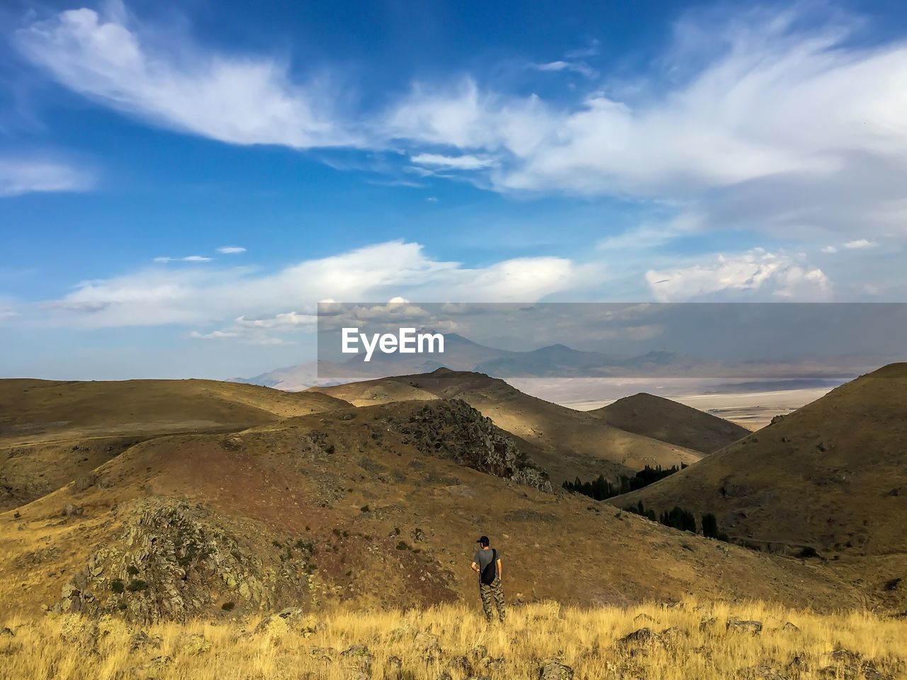 Rear view of man standing on landscape against cloudy sky