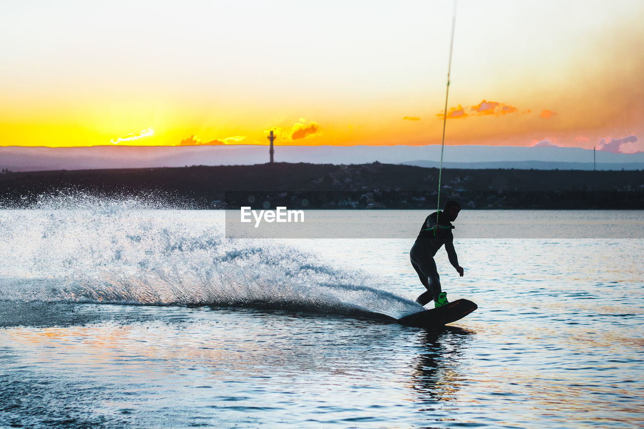 Wakeboarding man against sunset