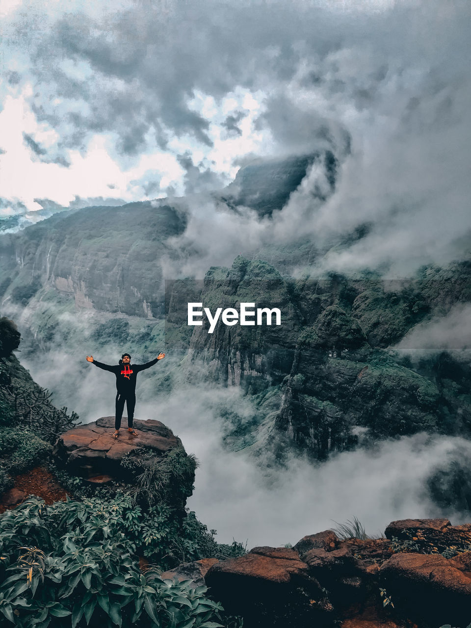 MAN STANDING ON ROCK BY MOUNTAIN