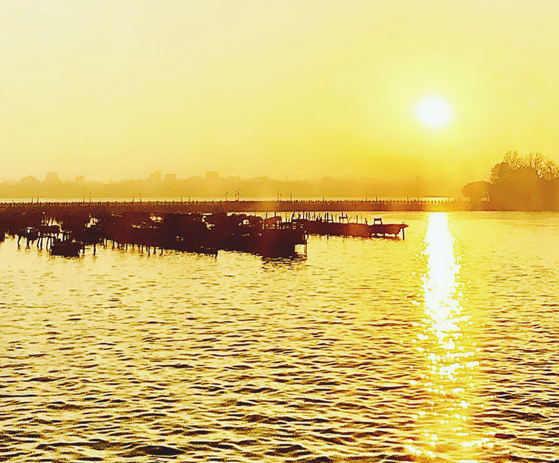 water, sky, sunset, nature, horizon, beauty in nature, dawn, evening, sea, sun, sunlight, reflection, scenics - nature, tranquility, nautical vessel, ship, transportation, shore, tranquil scene, no people, waterfront, outdoors, orange color, silhouette, idyllic, mode of transportation, vehicle, clear sky, lens flare, rippled, boat