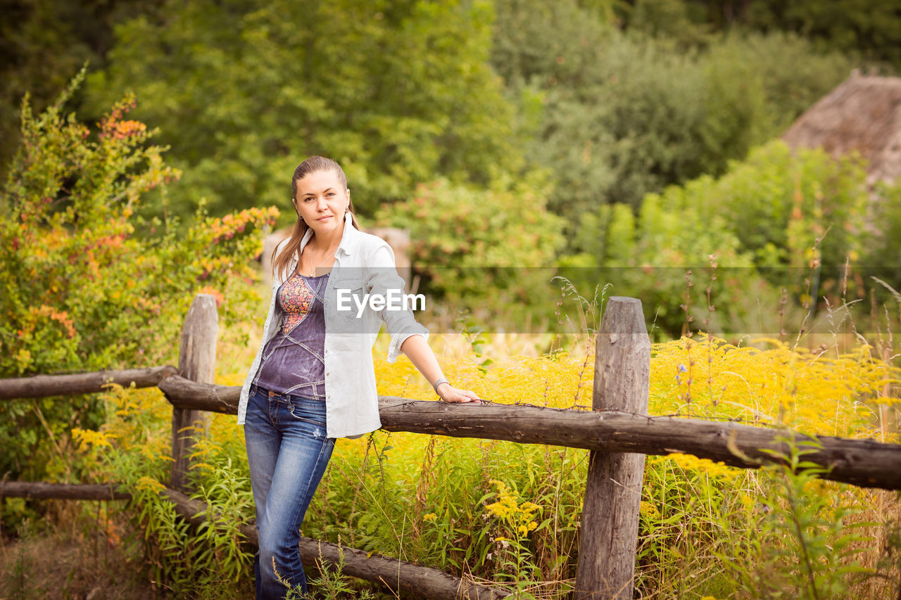 Attractive young woman standing near old wooden fence.