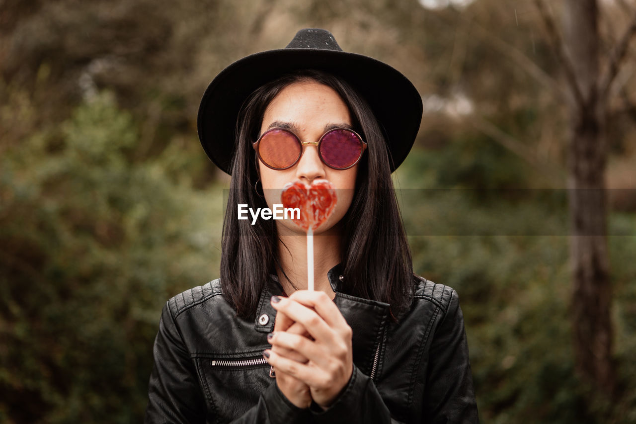 Portrait of woman wearing sunglasses holding heart shaped candy