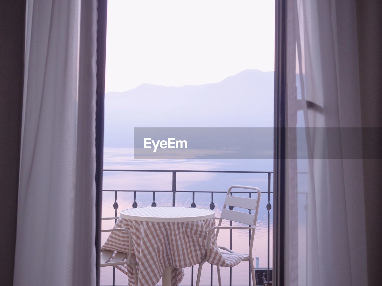 Empty chairs with table arranged in balcony against sea seen through window