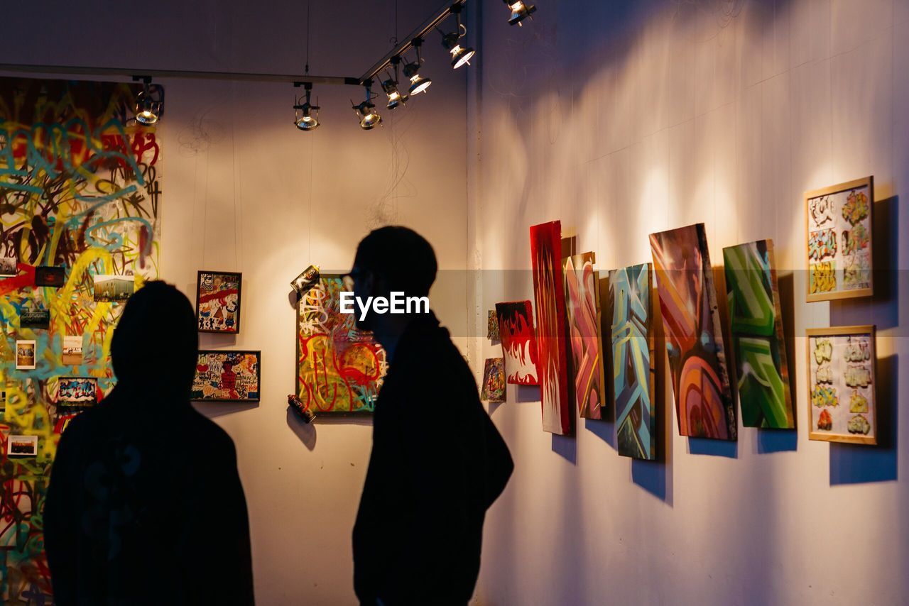 REAR VIEW OF WOMEN STANDING AGAINST WALL