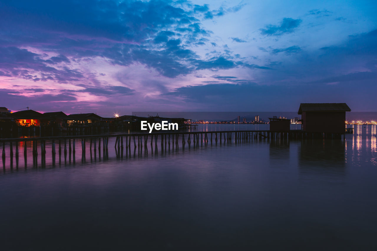 Scenic view of lake against illuminated buildings at sunset