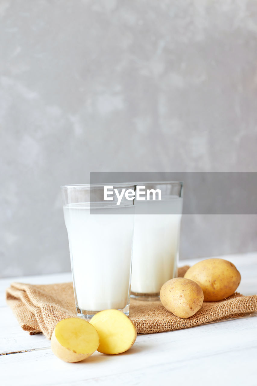 Potato milk in a glass mug stands on the table next to fresh potato tubers. alternative plant milk