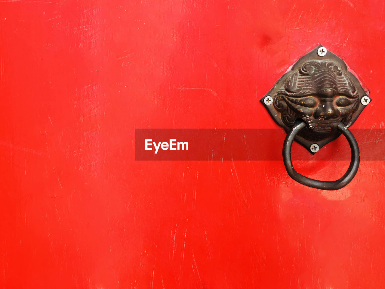 CLOSE-UP OF DOOR KNOCKER ON RED WALL WITH CLOSED DOORS