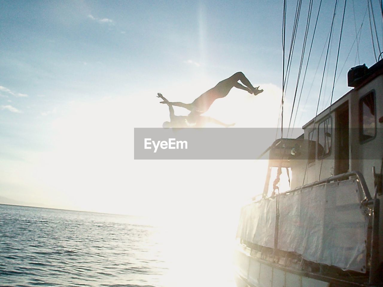 LOW ANGLE VIEW OF MAN JUMPING AT SEA AGAINST SKY