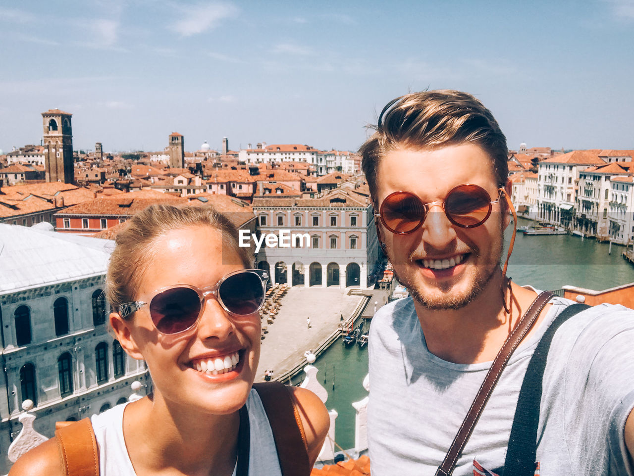 Portrait of smiling young couple standing in city against sky