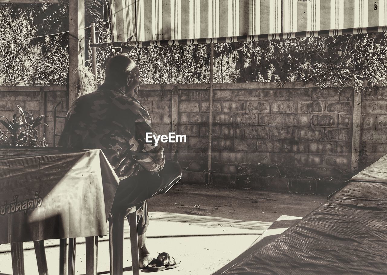 MAN LOOKING THROUGH WINDOW WHILE SITTING ON BUILDING