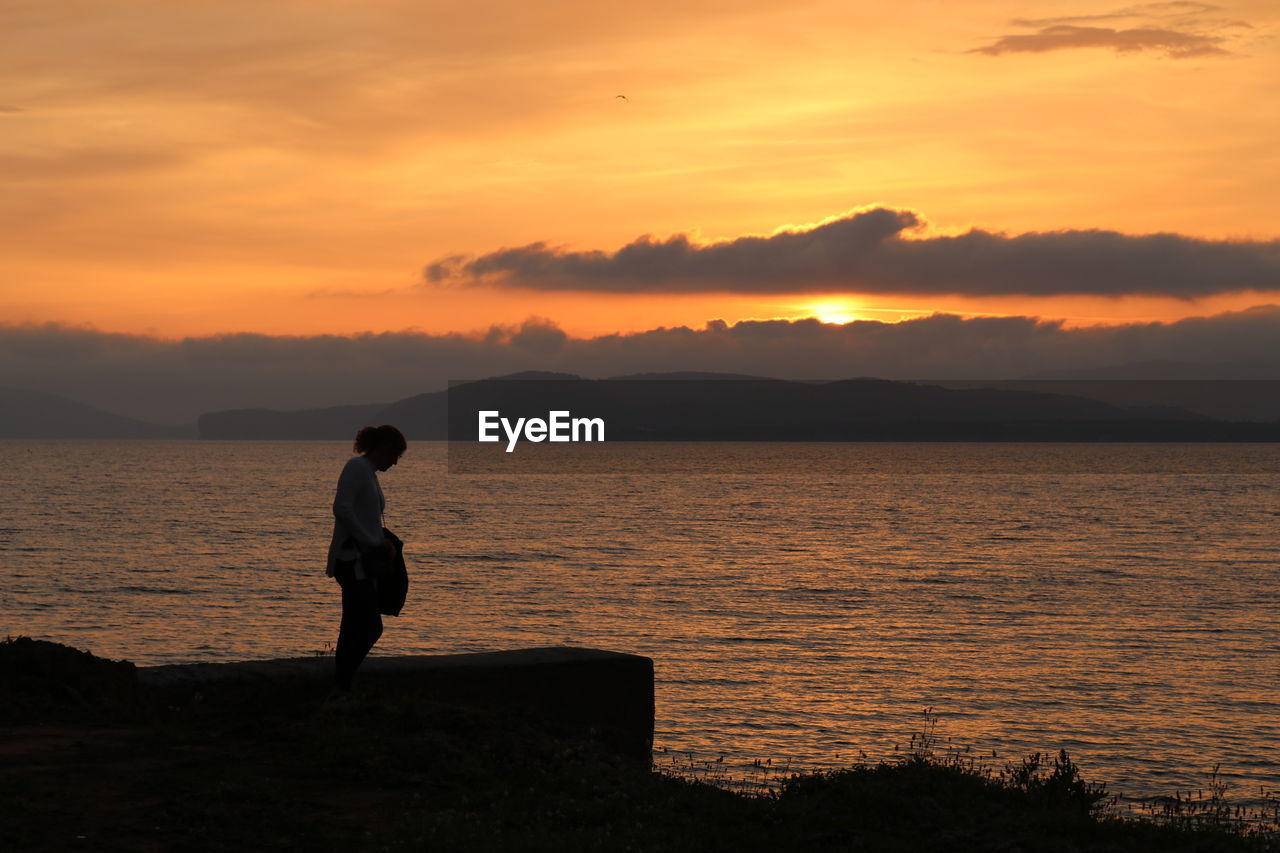 SILHOUETTE MAN LOOKING AT SEA DURING SUNSET