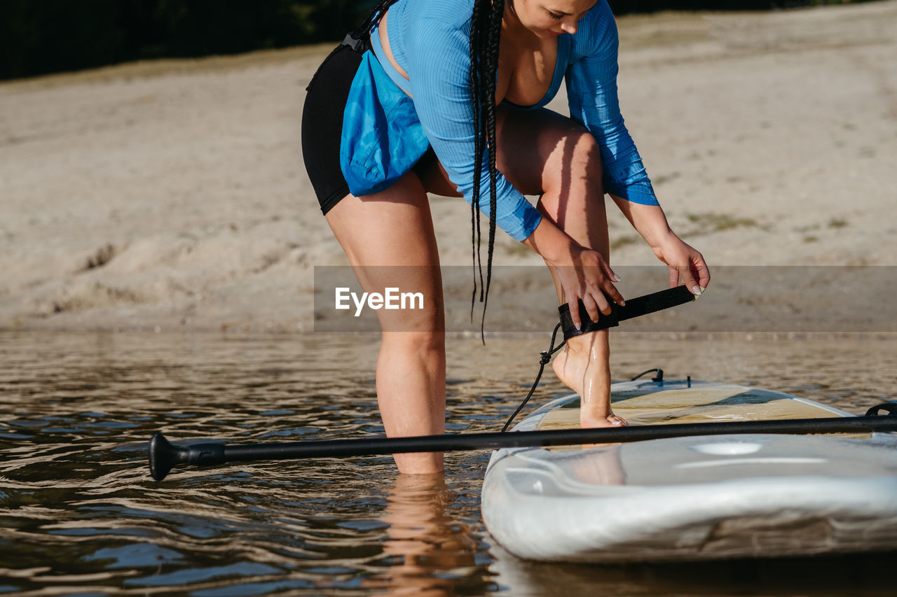 Woman attaching insurance cable of sup to her leg, preparing to swim on a board