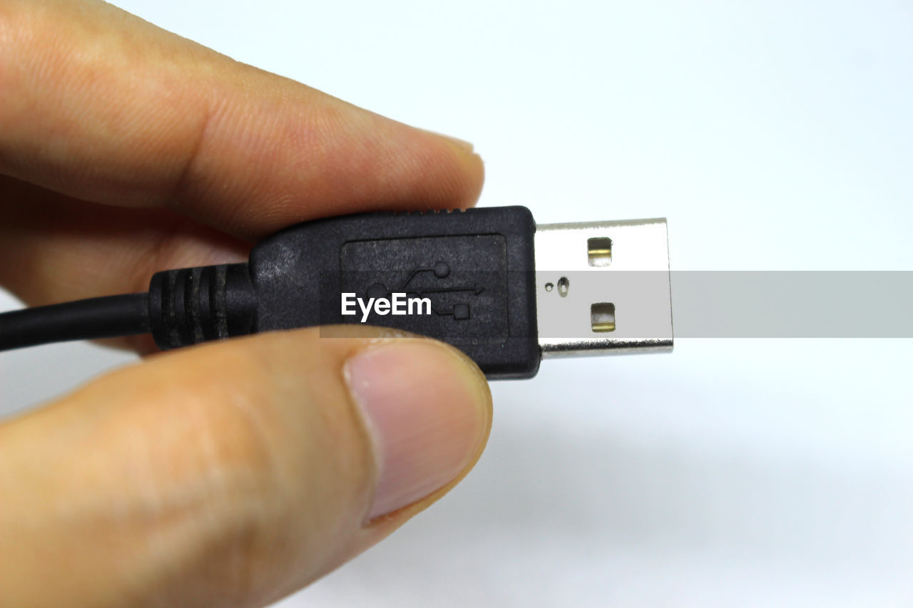 Close-up of person holding usb cable against white background