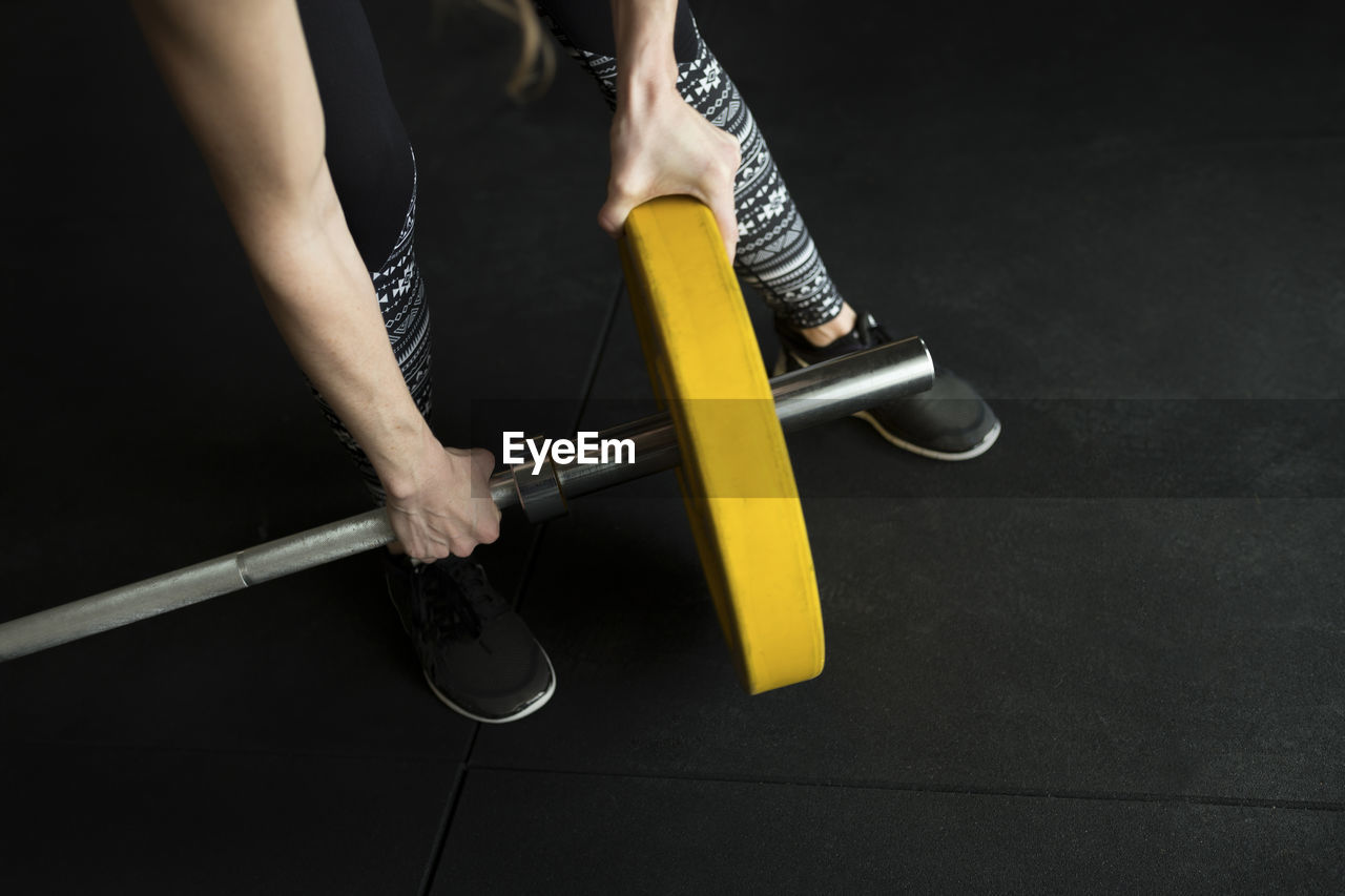 Low section of woman adjusting weight on barbell while exercising in gym