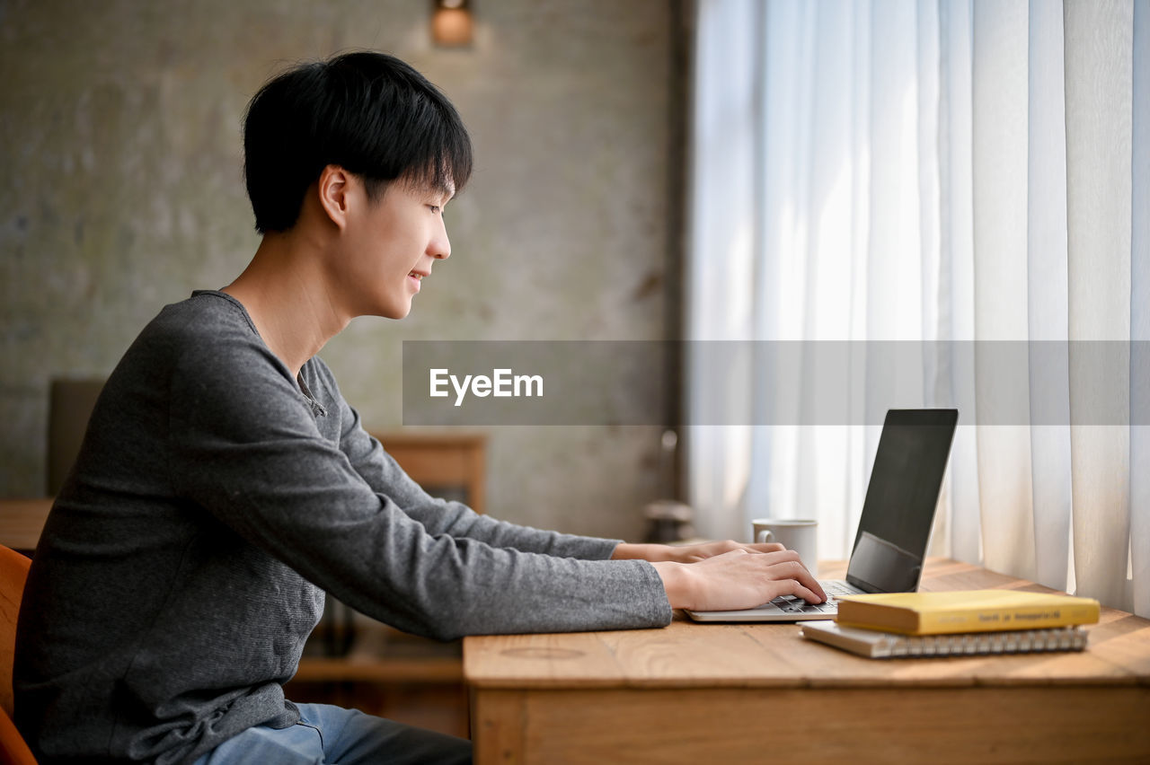 side view of young man using laptop while sitting at office
