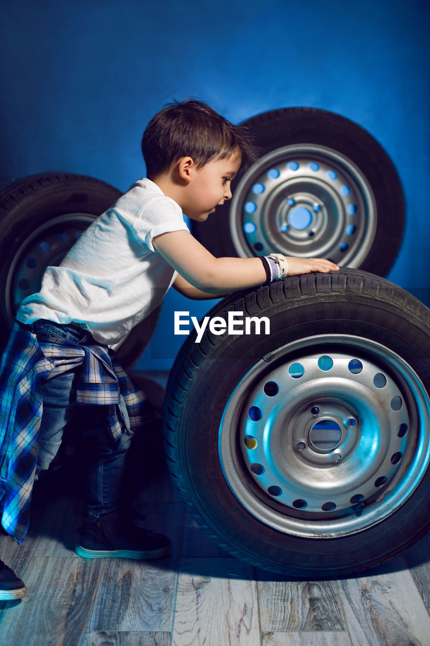 Boy in a white t shirt shirt and hat sits on a background of car wheels on a blue