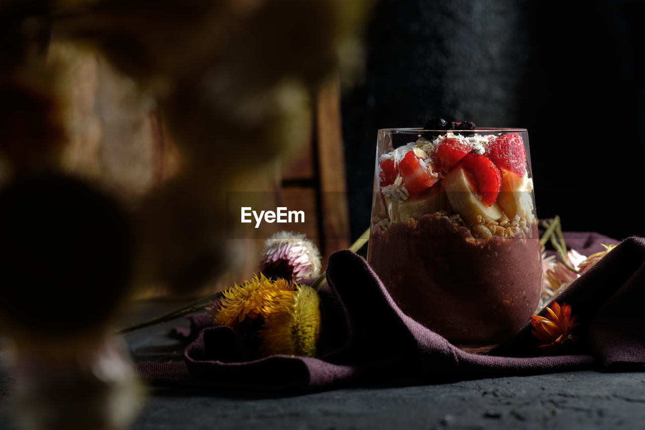 Appetizing smoothie bowl with granola strawberries and blueberries placed on table near various wildflowers