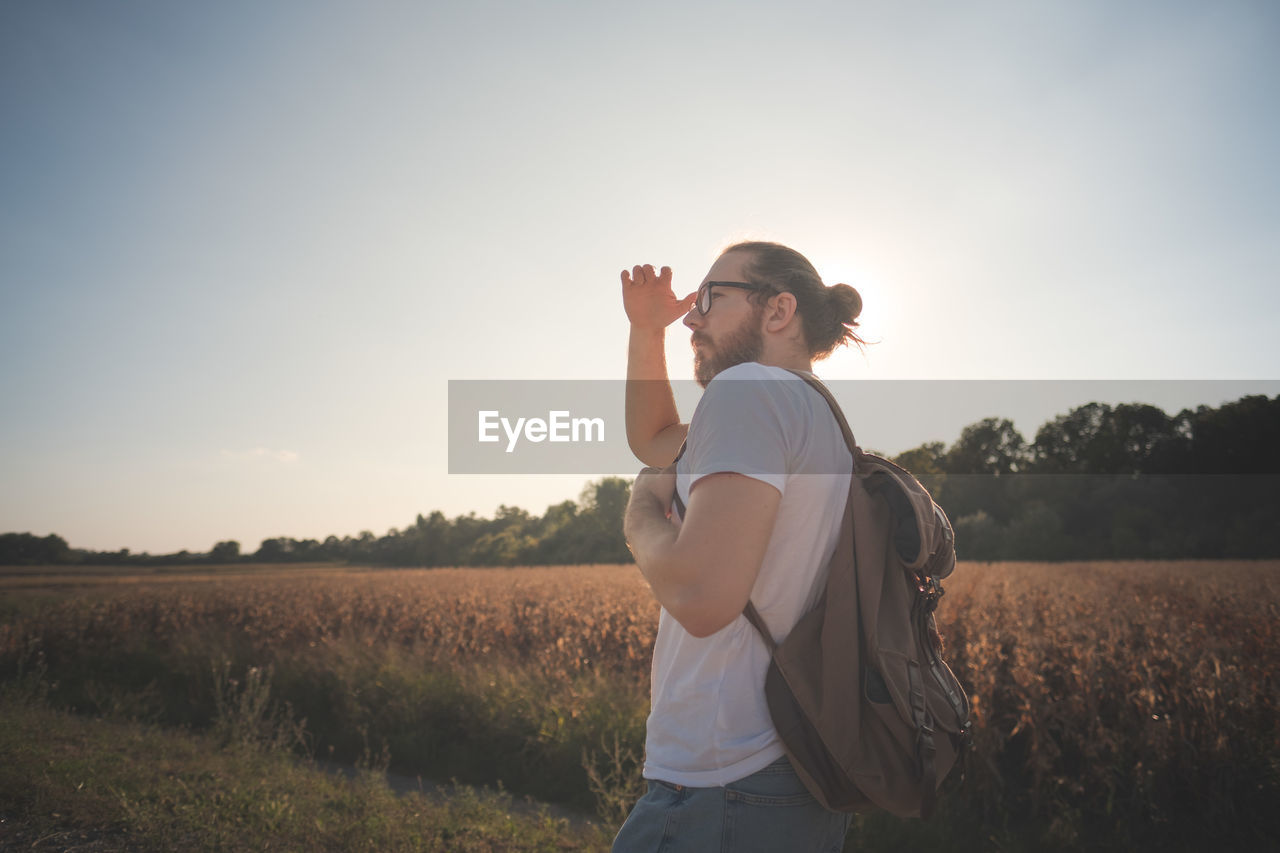 Man shielding eyes while standing on field against sky during sunset