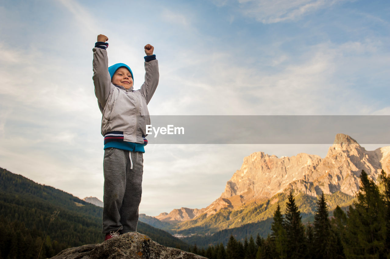 Low angle view of boy standing on mountain against sky