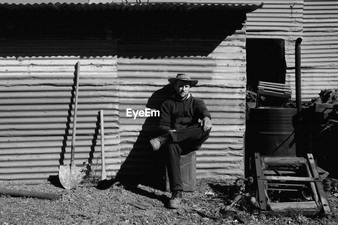 Full length of man sitting against abandoned house