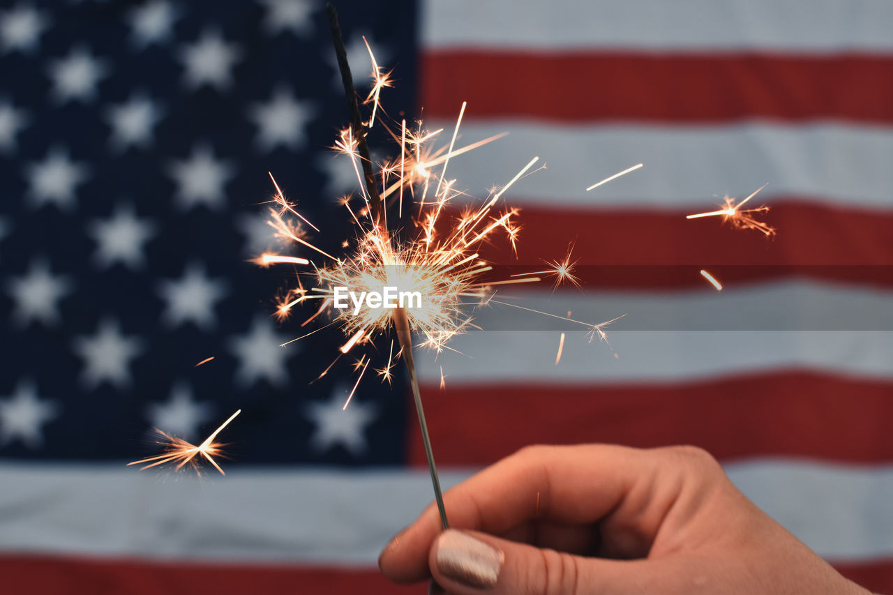 Cropped hand holding sparkler in front of usa flag 