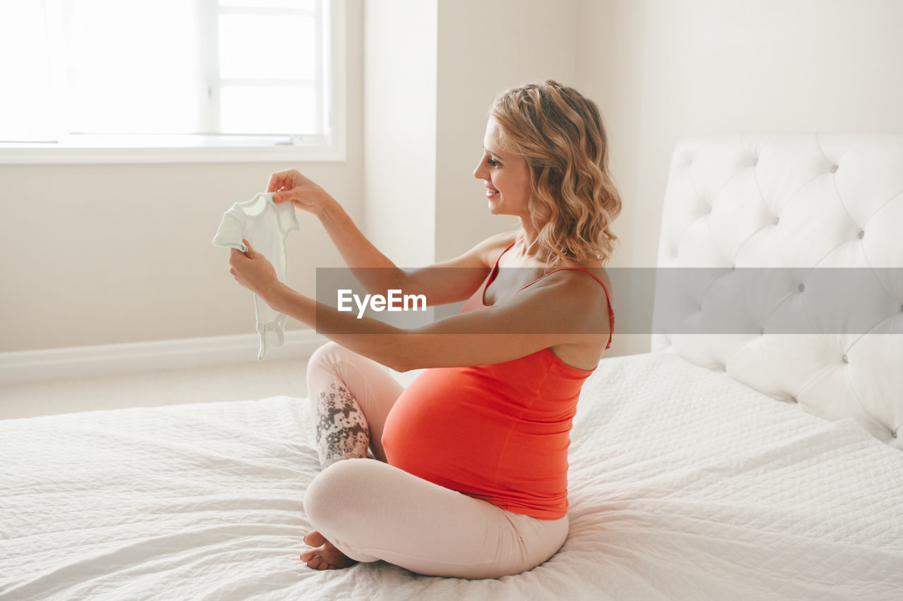 Side view of pregnant woman sitting on bed at home